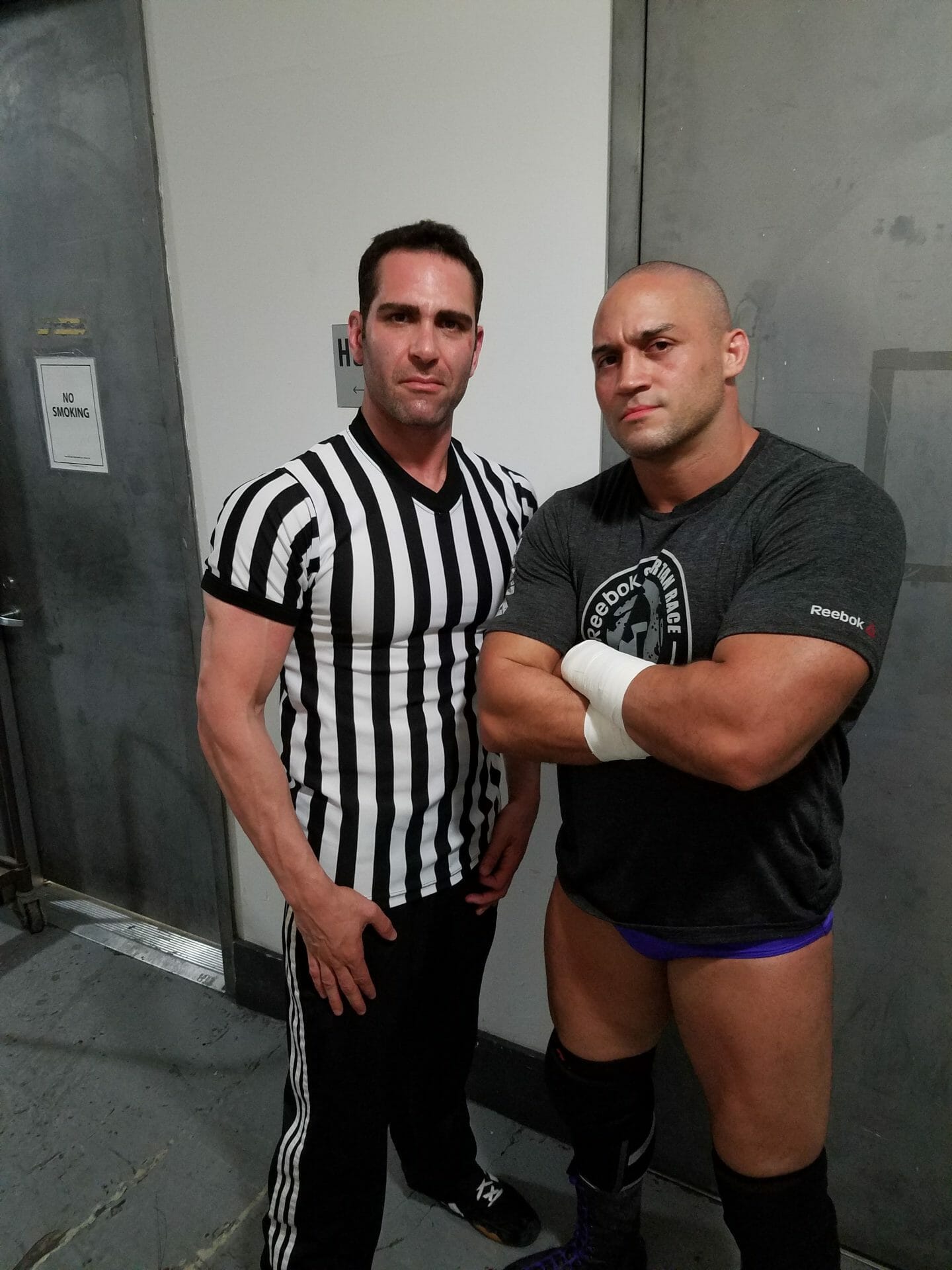 Israel Joffe in a striped referee shirt standing with a professional wrestler backstage in Brooklyn